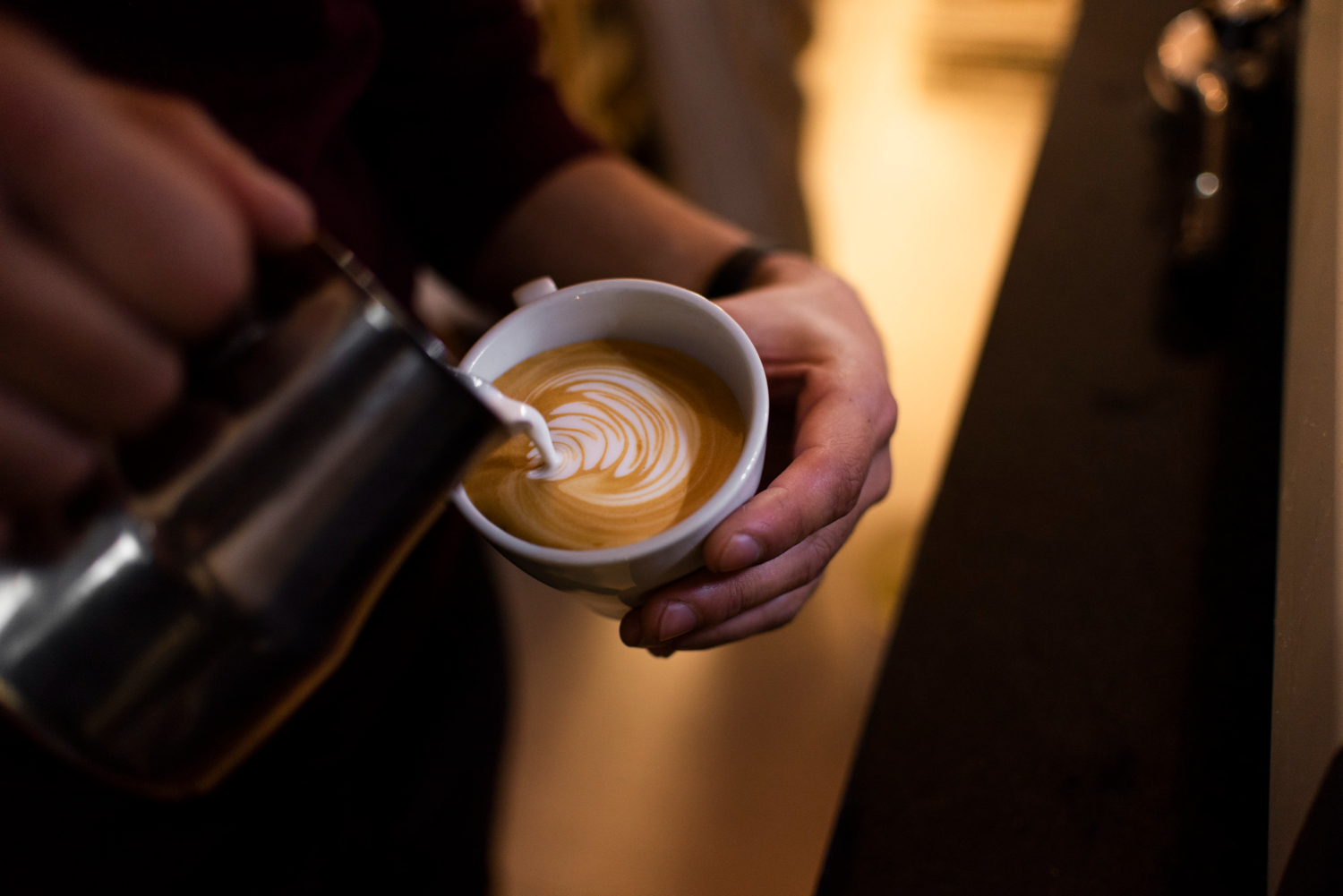 Επαγγελματίας bartender προσθέτει γάλα σε μια κούπα ζεστού cappuccino.